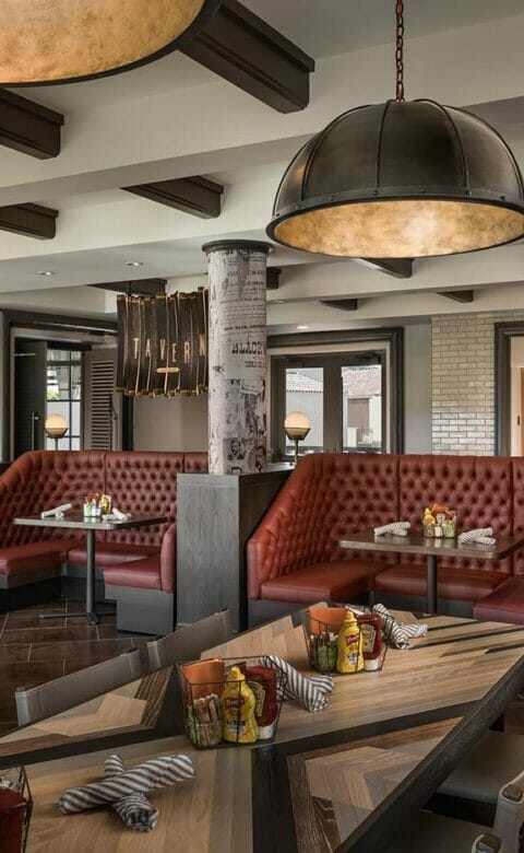 The Phoenician Tavern dining area with long striped table in the foreground and red leather booths in the background