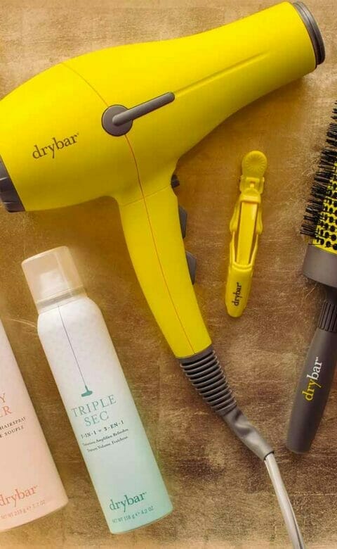 a Drybar hair dryer, brush, hair clips, and hair products laid out for display