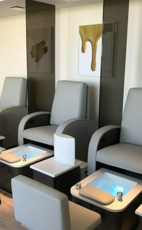 a row of spa chairs set up for pedicures with foot baths at their bases