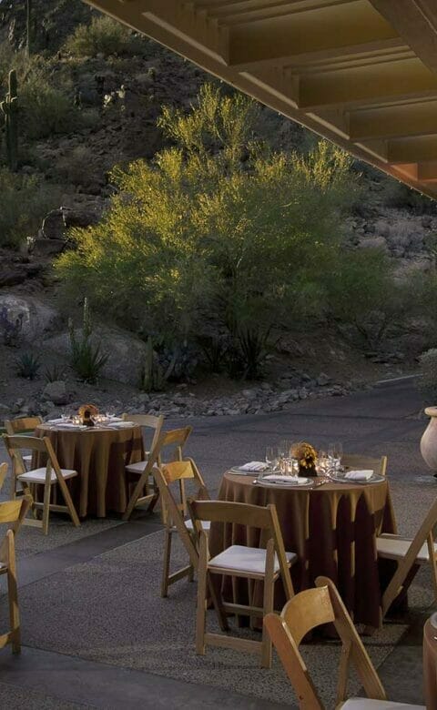 outdoor patio with four wooden chairs surrounding each of the five tables at night